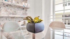 A modern interior with a glass table, two chairs, and a potted plant on a stand.