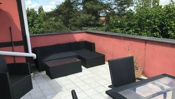 En tagterrasse med rød væg, sort fletningsmøbler og et glasbord.