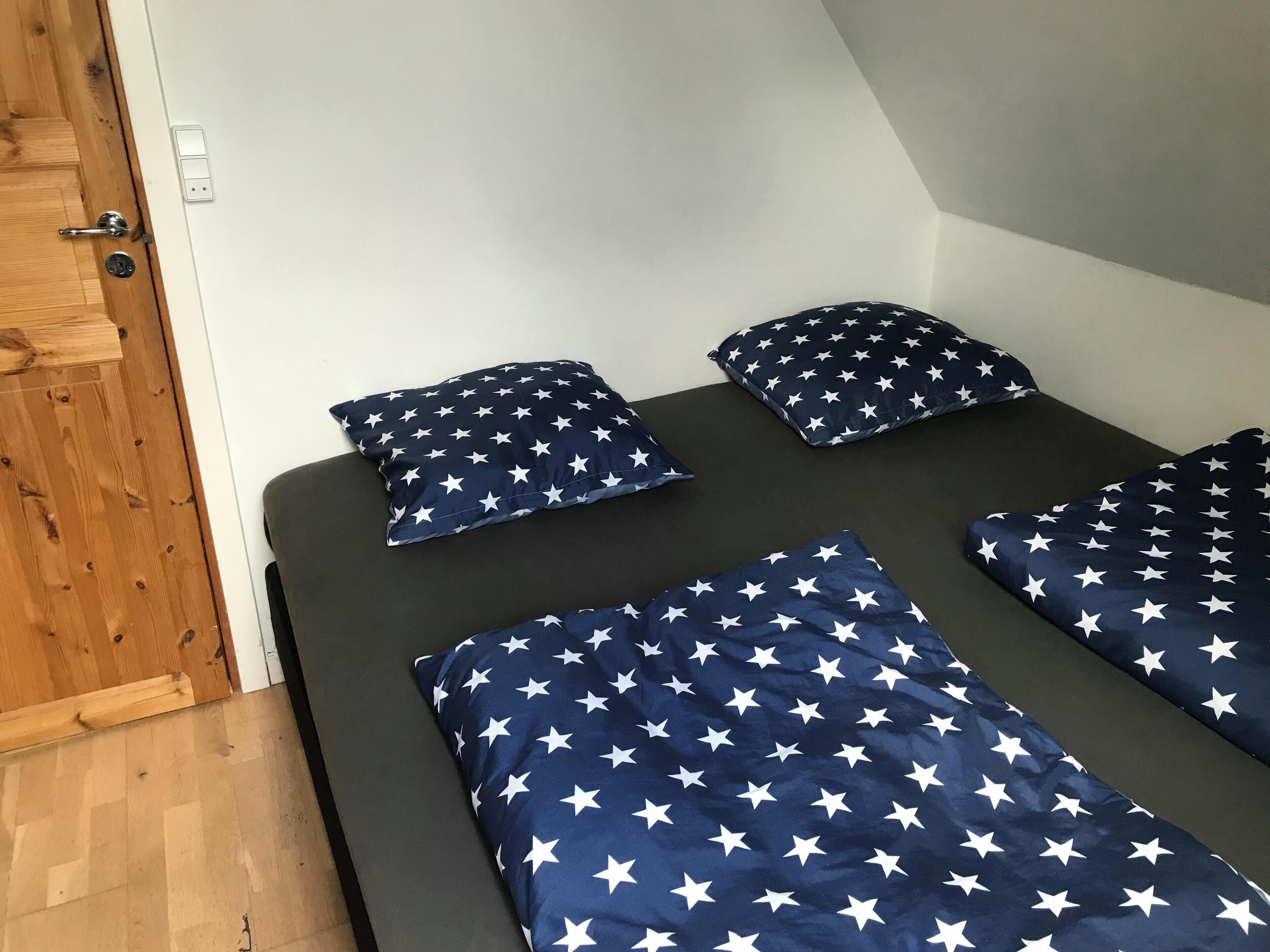 A room with a bed featuring a star-patterned bedspread, a wooden door, and a light switch on the wall.