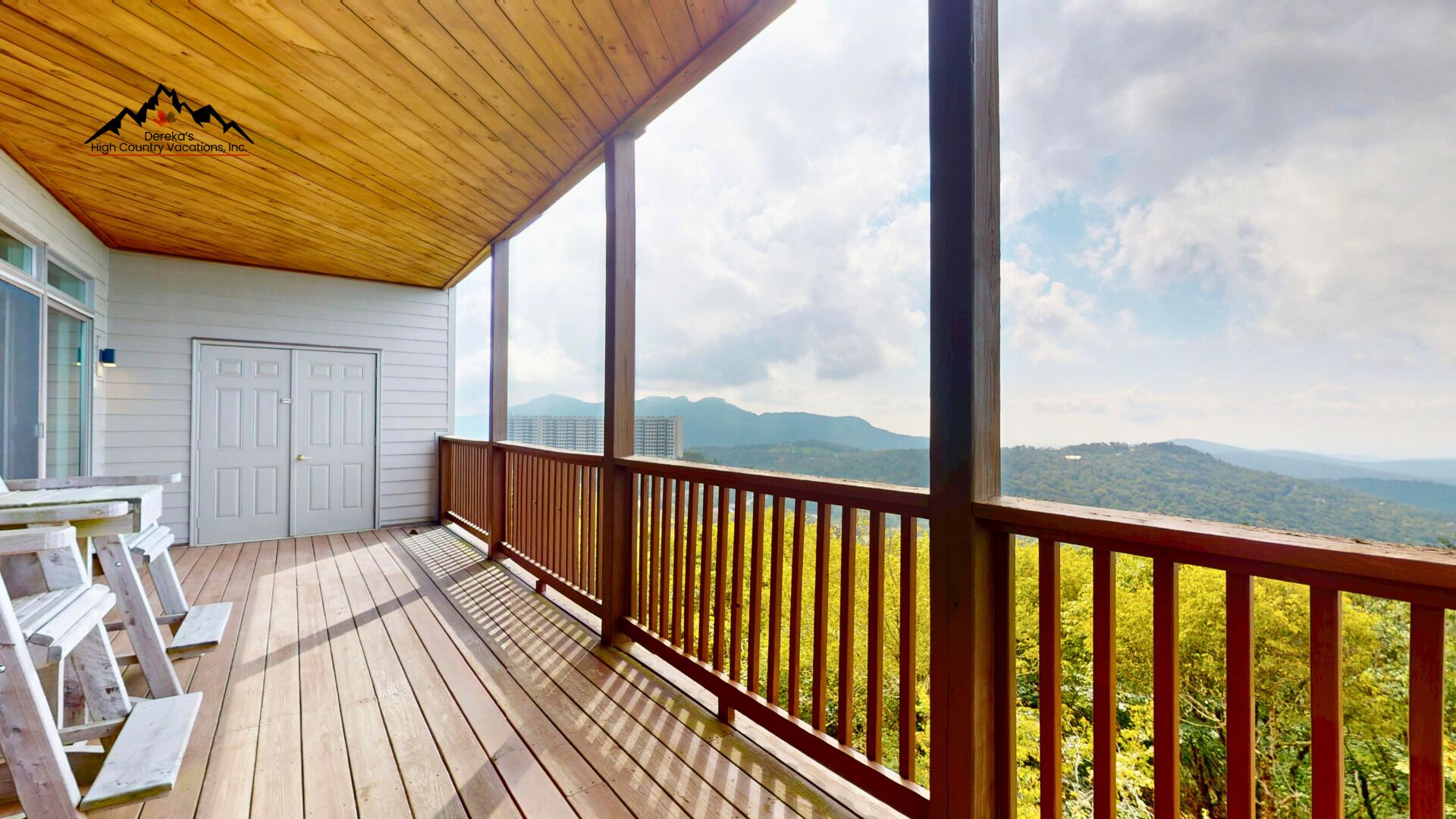 Eine Holzterrasse mit einer weißen Tür, einer Bank und Blick auf die Berge.