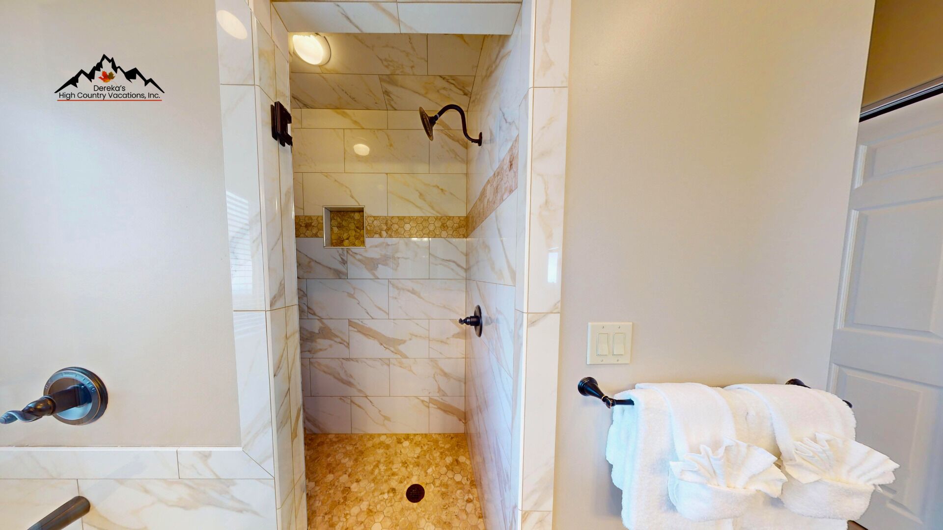 A bathroom with a shower area, marble tiles, a towel rack, and a logo on the wall.