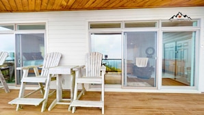 Un espace extérieur abrité comprenant deux fauteuils Adirondack, une terrasse en bois et une porte vitrée donnant accès à un espace intérieur.
