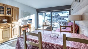 Une pièce chaleureuse comprenant une table à manger, des chaises, des meubles en bois et une grande fenêtre donnant sur des immeubles et des arbres.