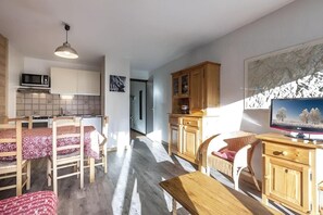 A compact living space with a kitchenette, a dining area with a table and chairs, a television, and a large window with a view.