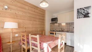 Une cuisine compacte aux murs en bois, une table à manger avec quatre chaises et un seul luminaire suspendu.