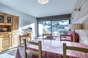 A room with a dining table, chairs, a wooden cabinet, and a large window offering a view of buildings.