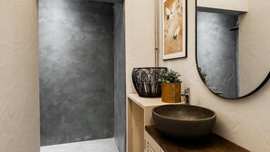 Ein modernes Badezimmer mit einem großen Spiegel, einem runden Waschbecken und einem gerahmten Kunstwerk an der Wand.