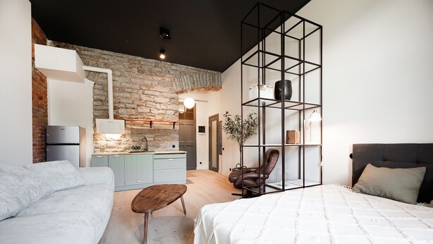 Ein modernes Schlafzimmer mit Bett, Sessel, Sofa und einer kleinen Küchenzeile im Hintergrund.