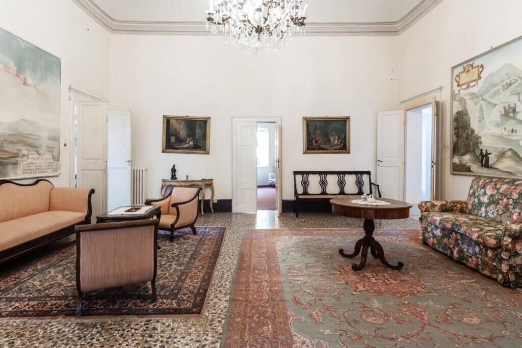 A spacious room with a large chandelier, a sofa, a chair, a table, and a rug.
