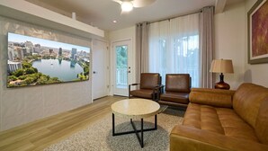 Sala de estar com vista para a cidade, ventilador de teto, mesa de centro redonda, sofá de couro marrom e luminária.