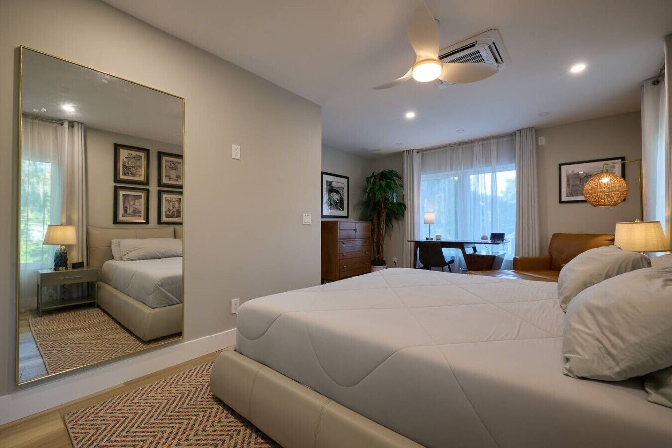 Une chambre d’hôtel avec un grand lit, un bureau, une chaise, une commode et un grand miroir.