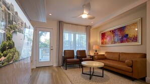 Uma sala de estar moderna com sofá, cadeiras, mesa de centro, ventilador de teto e uma janela grande com vista para a cidade.
