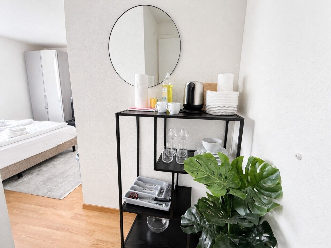 A hotel room with a bed, a black metal side table with a mirror, and a potted plant.