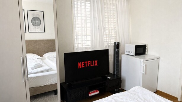 A hotel room with a bed, a television displaying 'NETFLIX,' a microwave, and a refrigerator. - Charming Riverside Studio - Stork 41 (Zürich)