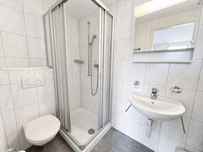 A modern bathroom with a glass-enclosed shower, a white toilet, and a pedestal sink. - Charming Riverside Studio - Stork 41 (Zürich)
