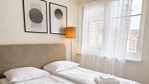Un lit double avec du linge de lit et des serviettes blanches, une tête de lit, une lampe sur pied et deux œuvres d’art encadrées accrochées au mur.