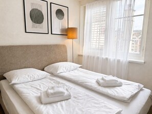 A double bed with white linens and towels, a headboard, a floor lamp, and two framed artworks on the wall. - Charming Riverside Studio - Stork 41 (Zürich)
