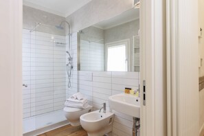 Un baño moderno con ducha envuelta en vidrio, lavamanos doble y un inodoro.
