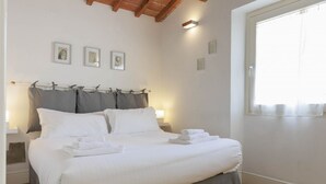 A neatly made bed with white linens and grey bedding, a wooden ceiling, and a window with sheer curtains. - Santa Maria Novella Top Floor Hideaway (Firenze)