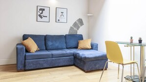 A blue sectional sofa with two pillows, a yellow chair, and a glass table with two potted plants. - Santa Maria Novella Top Floor Hideaway (Firenze)