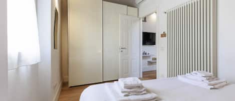 A bedroom with a bed, white towels, a wardrobe, a radiator, and a TV.