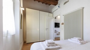 A bedroom with a bed, white towels, a wardrobe, a radiator, and a TV. - Santa Maria Novella Top Floor Hideaway (Firenze)