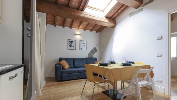 A dining area with a table, chairs, and a sofa in a room with wooden flooring and a sloped ceiling. - Santa Maria Novella Top Floor Hideaway (Firenze)