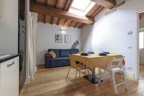 A dining area with a table, chairs, and a sofa in a room with wooden flooring and a sloped ceiling. - Santa Maria Novella Top Floor Hideaway (Firenze)