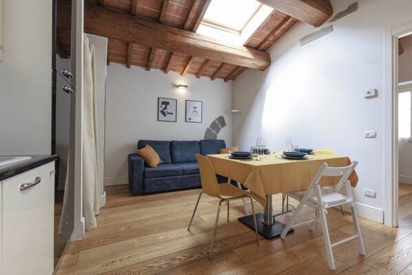 Un área de comedor con una mesa, sillas y un sofá en una habitación con suelo de madera y techo inclinado.