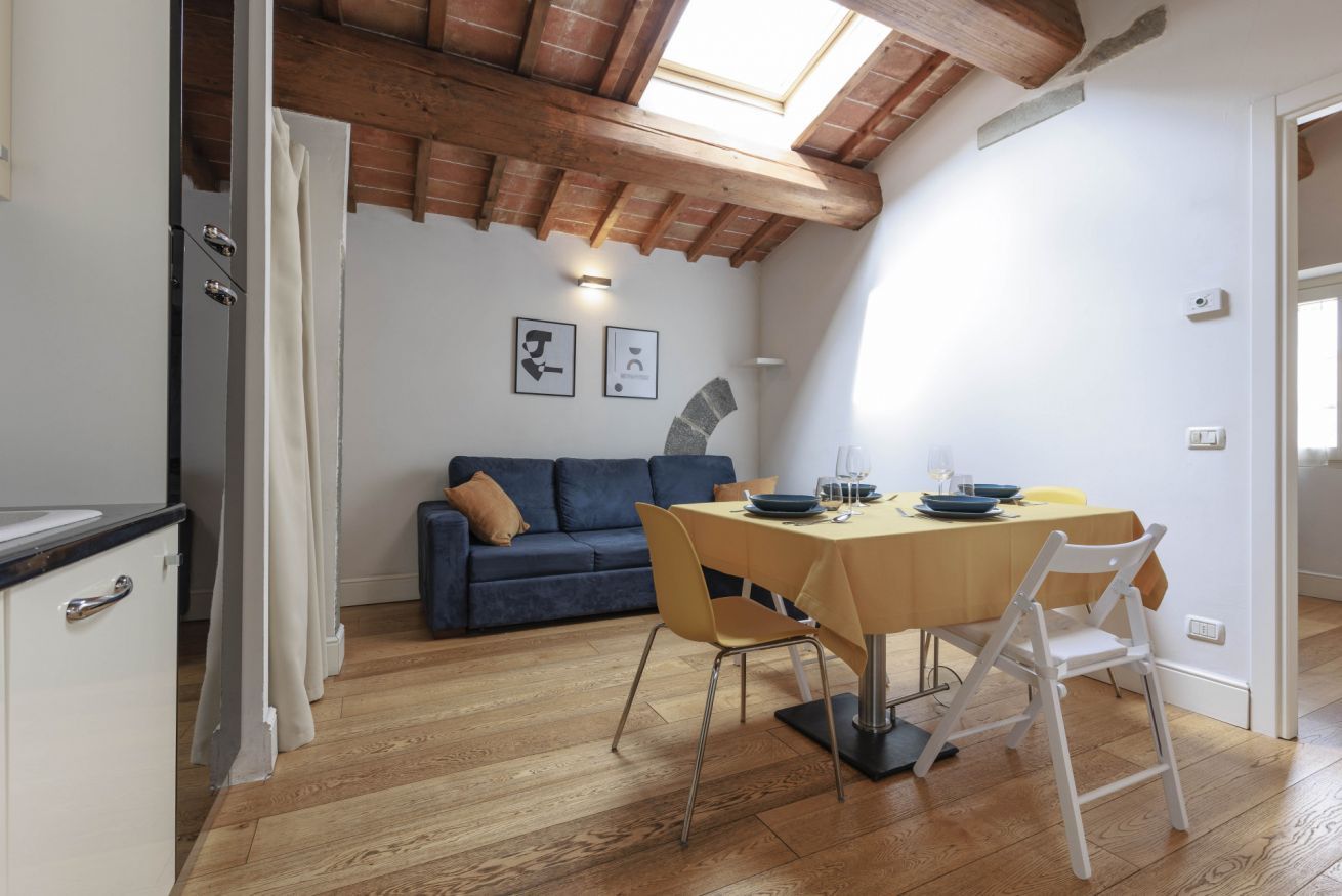 Un espace repas comprenant une table, des chaises et un canapé, situé dans une pièce au plancher en bois et au plafond en pente.