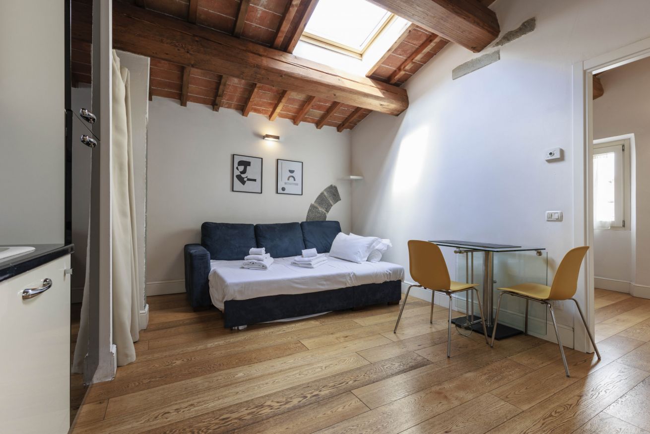 Ein kleines Zimmer mit einem Bett, einem Tisch und zwei Stühlen. Über dem Bett befindet sich ein Oberlicht und zur Rechten ein kleines Fenster.