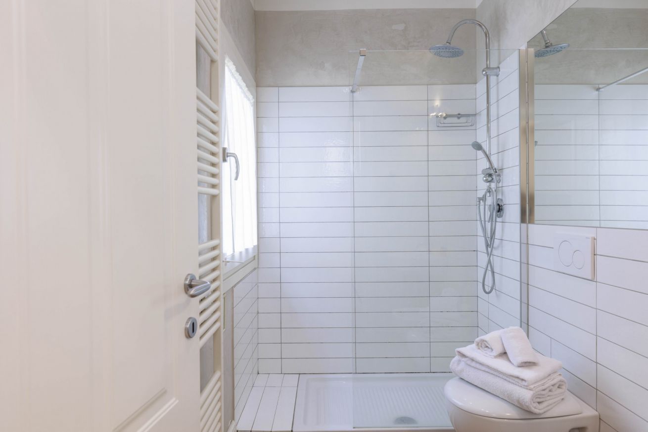 A modern bathroom with white tiles, a glass shower enclosure, a toilet, and a towel stack.