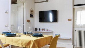 A dining area with a table set for four, a flat-screen TV mounted on the wall, and a shelf with small decorative items. - Santa Maria Novella Top Floor Hideaway (Firenze)