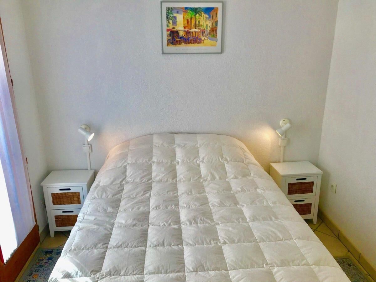 A bedroom with a large bed, two bedside tables with lamps, a small nightstand, and a framed picture on the wall.