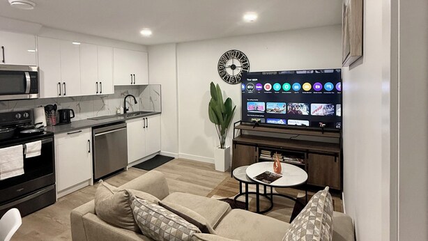 A modern living room with a beige sofa, a coffee table, and a flat-screen TV mounted on the wall. - Cozy 2 Bedroom Suite Close to Amenities (Edmonton)