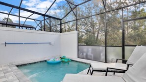 An indoor swimming pool with clear glass walls, lounge chairs, and inflatable toys.