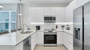 A modern kitchen with white cabinetry, a built-in microwave, a stainless steel refrigerator, and a central island with a sink and seating.