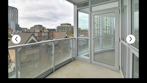 Un balcon doté d’une porte vitrée et d’une rambarde en métal, offrant une vue sur un paysage urbain composé de différents bâtiments.