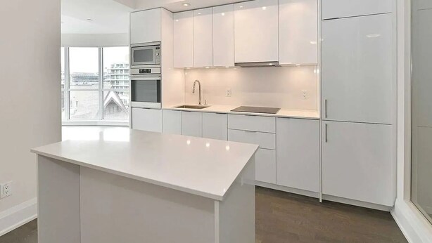 Une cuisine moderne avec des meubles blancs, un îlot central, des appareils électroménagers intégrés et une grande fenêtre offrant une vue sur la ville.