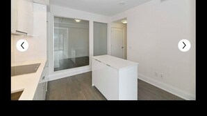 Un couloir moderne et bien éclairé, avec un comptoir d’accueil blanc, une porte en verre donnant sur une autre pièce et un mur blanc avec une porte sur le côté droit.