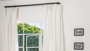 A bedroom with a bed, a chair, a window with curtains, and two framed pictures on the wall.