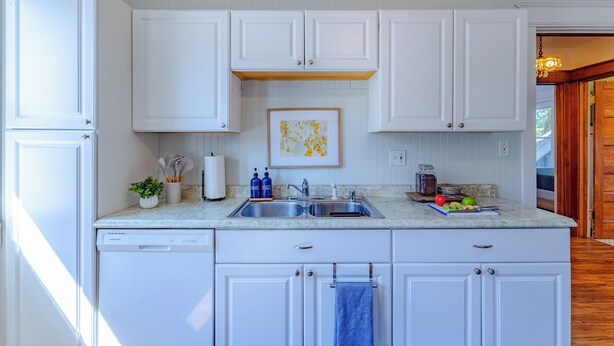 A kitchen with white cabinets, a double sink, and a countertop with various items.