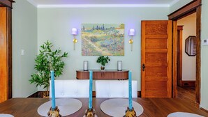 Un coin repas avec une table en bois, trois chandeliers, une plante en pot, un tableau accroché au mur et un banc.
