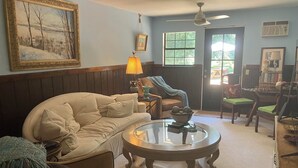 A cozy living room with a beige sofa, a glass coffee table, and a fireplace. There are two windows with curtains, a ceiling fan, and a framed painting on the wall. - Beautiful accommodation for a peaceful stay, close to W.E.C. Gainesville, Ocala. (Citra)