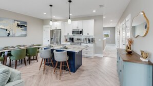 Une cuisine moderne avec des meubles blancs, un îlot central et des luminaires suspendus.