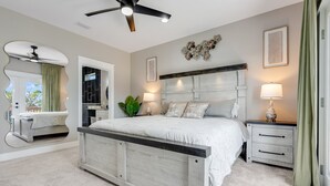 Une chambre à coucher avec un grand lit, un ventilateur de plafond, une table de chevet avec une lampe et un miroir fixé au mur.