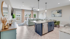 Une cuisine moderne dotée d’un îlot central, d’appareils électroménagers intégrés et de luminaires suspendus.