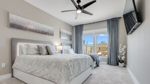 A bedroom with a large bed, a ceiling fan, and a view of the outside.