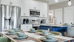 A modern kitchen with white cabinets, stainless steel appliances, and a dining area set with blue plates and bowls.
