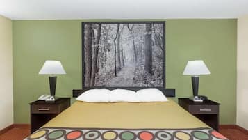 A hotel room with a bed, two bedside tables with lamps, a telephone, and a large forest-themed artwork on the wall.